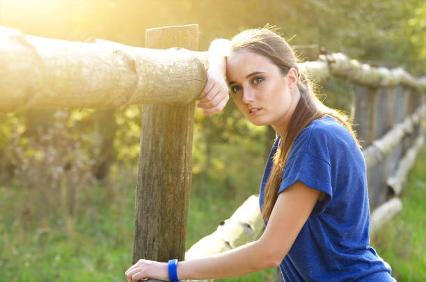 Young tired woman having a rest near wooden fence after jogging outdoors summer time. Healthy lifestyle concept