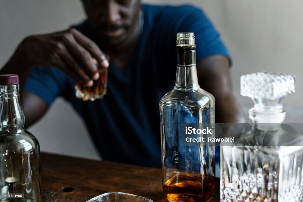 African descent man sitting drinking whiskey alcoholic addiction bad habit ***NOTE TO INSPECTOR: Please re-submit again.*** Alcohol Abuse Stock Photo