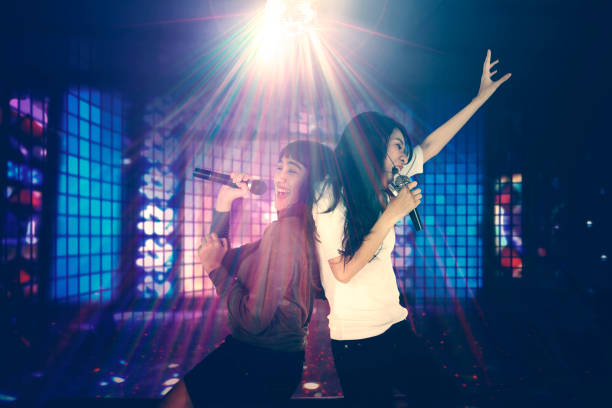 Two women singing in the night club Two women having fun together in the night club while singing under a disco ball with bright rays karaoke stock pictures, royalty-free photos & images