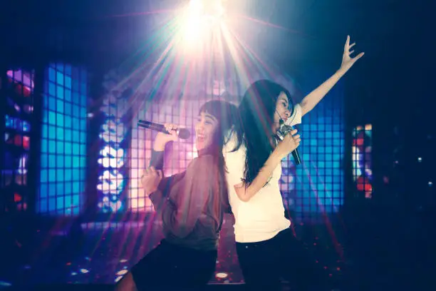 Two women having fun together in the night club while singing under a disco ball with bright rays