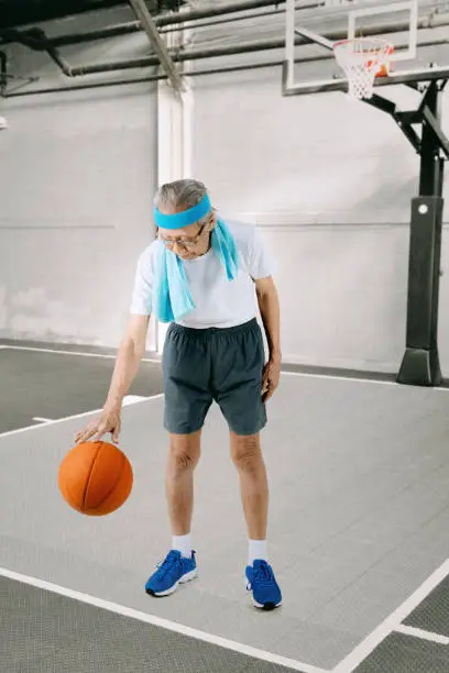 Portrait of an elderly man wearing sportswear while dribbling a basketball in the stadium