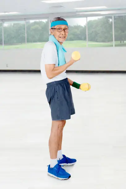 Full length of an elderly man wearing sportswear while training with two dumbbells