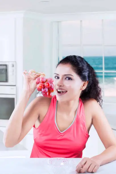 Image of young woman holding a bunch of ripe grapes while smiling and looking at the camera