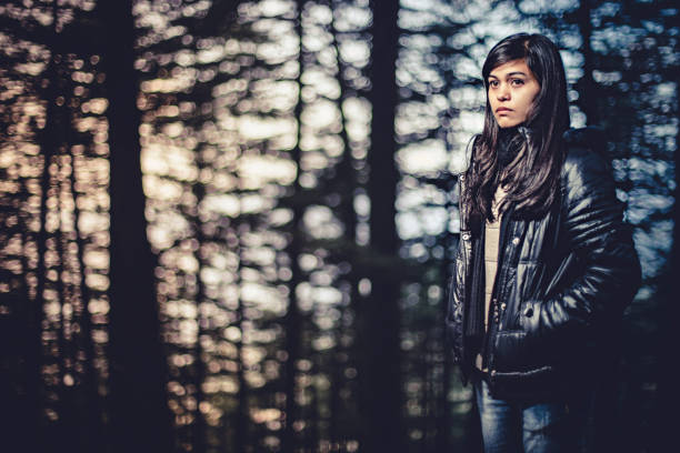Outdoor image of beautiful serene Asian young woman standing in woodland of pine trees. She is wearing warm cloths. One person, three quarter length and selective focus with copy space. Image taken in Solan, Himachal Pradesh.
