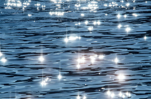 This abstract image features a mesmerizing bokeh effect created by sunlight reflecting on a water surface. The bright, shimmering circles create a dreamy and ethereal atmosphere, perfect for backgrounds or conceptual designs.
