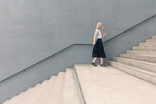 Young happy woman walking on stairs by concrete wall