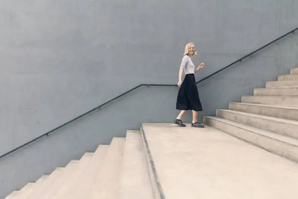 Photo of Young happy woman walking on stairs by concrete wall