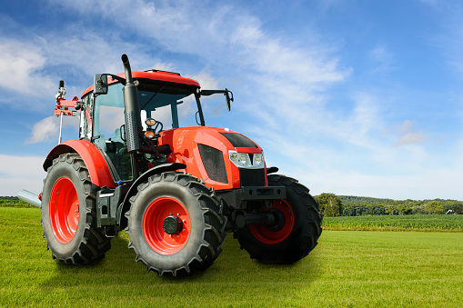 Composite image of a modern red agricultural generic tractor on a green field on a sunny day.