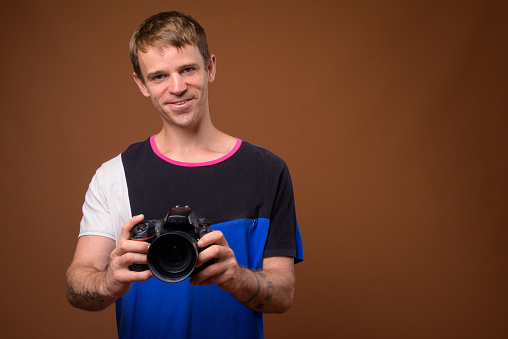 Studio shot of man with camera wearing multi colored shirt against colored background horizontal shot
