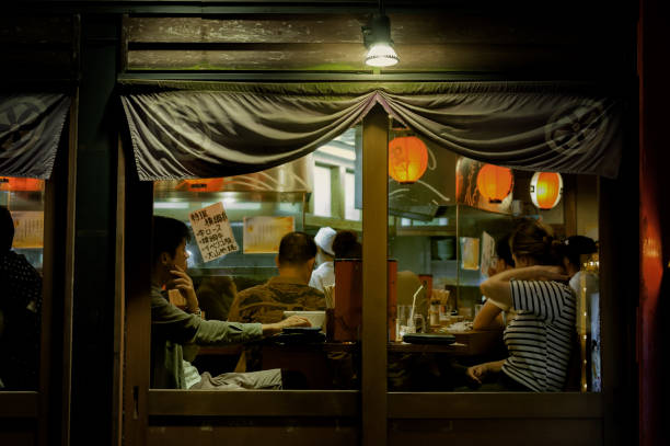 KYOTO, JAPAN - October 18, 2016: A typical setting in a local Japanese restaurant. Some would sit next to counter on which the chef prepare meals, others prefer sitting elsewhere. A couple sat by the window have already finished the meals and been waiting to pay their bills.