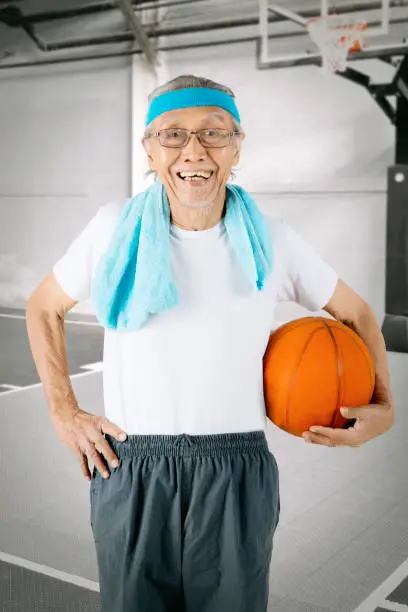 Portrait of a cheerful elderly man carrying a basketball while standing on the basketball court