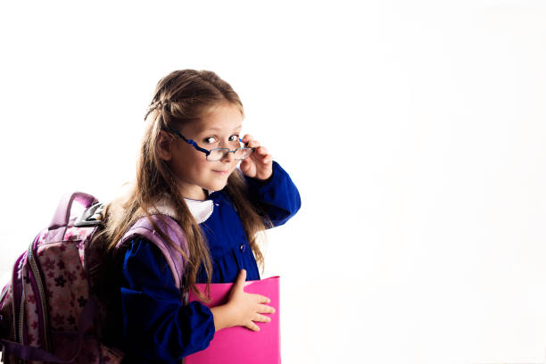 Caucasian elementary age schoolgirl with glasses posing in uniform and backpack on white background. School and education concept.