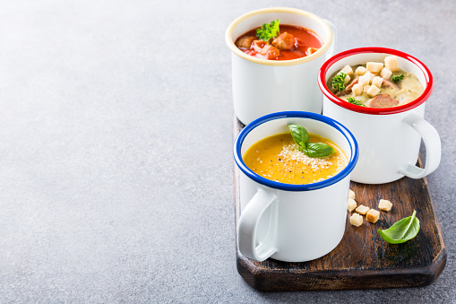 Assorted delicious homemade soups in enamel mugs with ingredients. Healthy food concept with copy space.