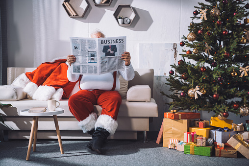 obscured viewof santa claus reading business newspaper while sitting on sofa
