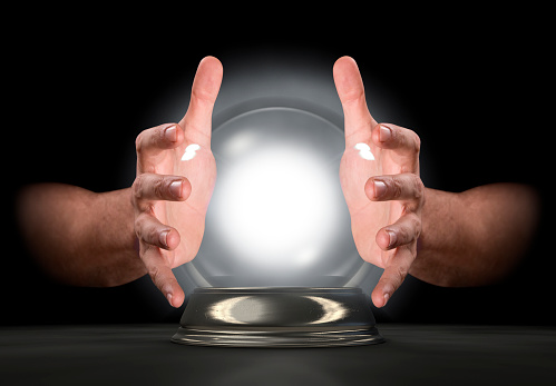 A pair of male hands surrounding a crystal ball on an isolated dark studio background