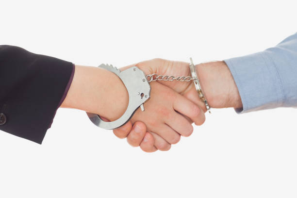 Closeup of business people in handcuffs shaking hands against white background