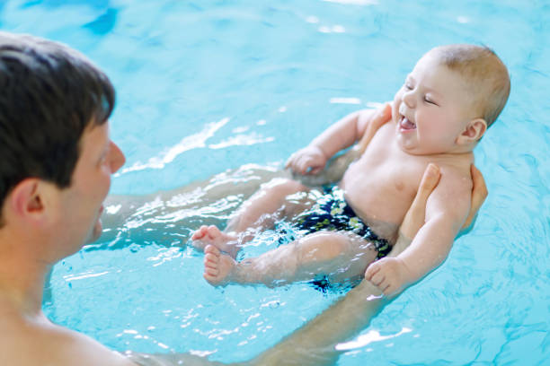padre de mediana edad feliz nadando con lindo bebé adorable en piscina. - bebe bañandose fotografías e imágenes de stock