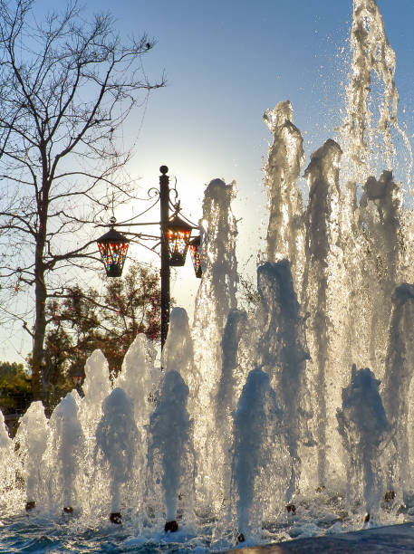 Water jets go upwards in outdoors water fountain with sunset sky back light.