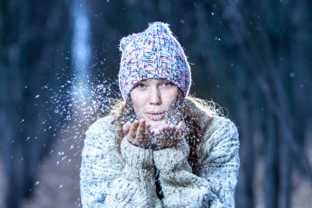 very beautiful girl blowing snow from her palms in the forest