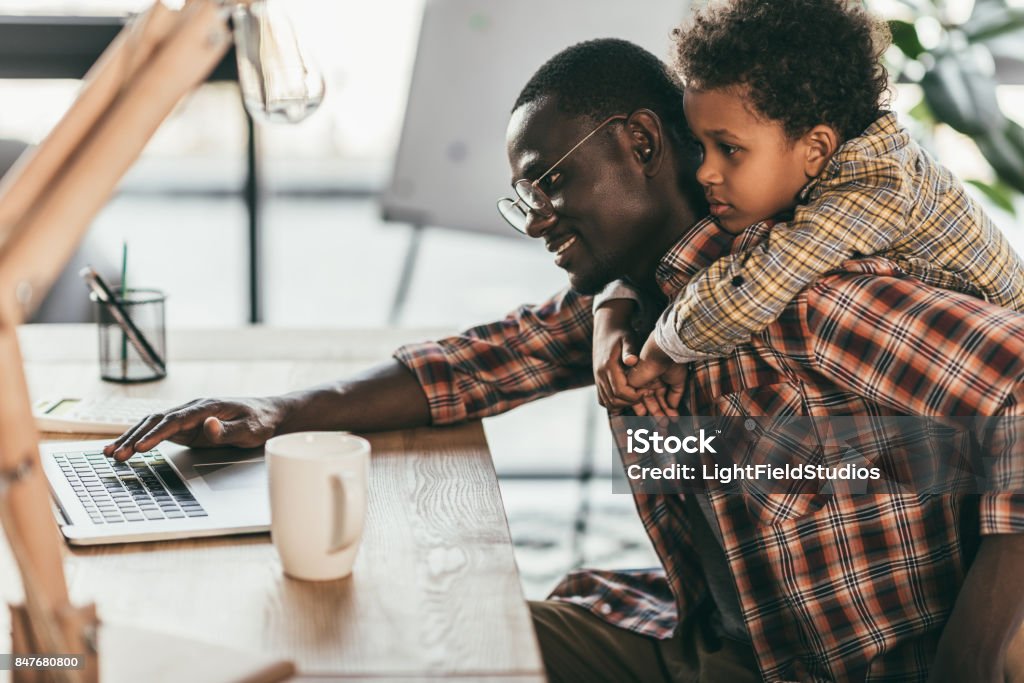 father and son using laptop in office side view of smiling african-american father and son using laptop in office Life Balance Stock Photo