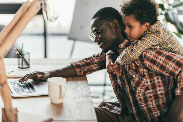 father and son using laptop in office side view of smiling african-american father and son using laptop in office life balance photos stock pictures, royalty-free photos & images