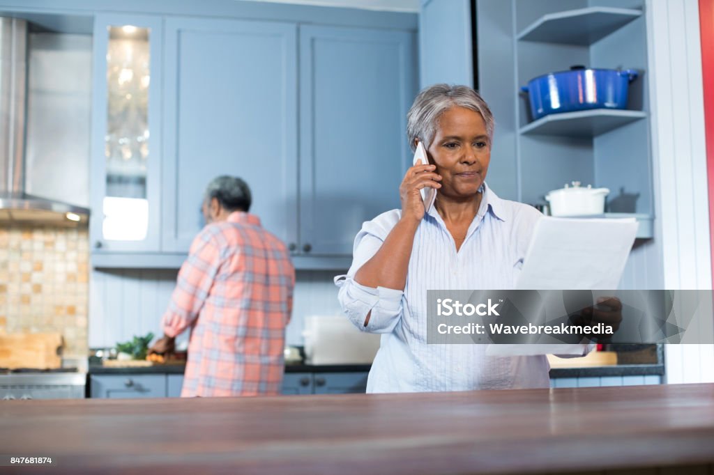 Woman reading document while standing in kitchen Woman reading document while standing in kitchen at home Rear View Stock Photo