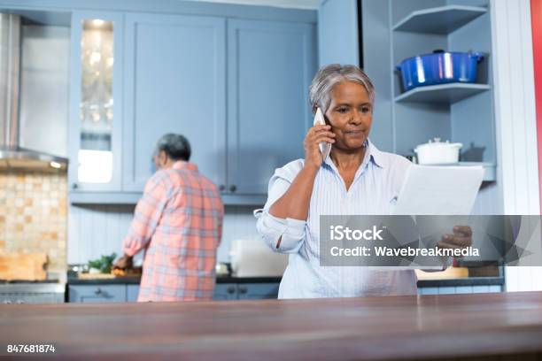 Woman Reading Document While Standing In Kitchen Stock Photo - Download Image Now - Rear View, Senior Men, Talking
