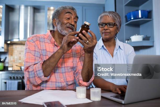 Man Looking At Medicine While Sitting By Woman Using Laptop Stock Photo - Download Image Now