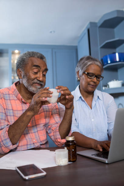 istock Man looking at medicine while sitting by woman using laptop computer 847682546