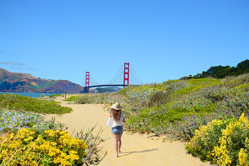Woman on hiking trip,girl walking on pathway enjoying beautiful coastal  landscape.  Golden Gate Bridge, over Pacific Ocean and San Francisco Bay, Baker Beach, San Francisco, California, USA