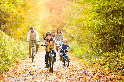 Beautiful young family with two sons in warm clothes cycling outside in autumn nature