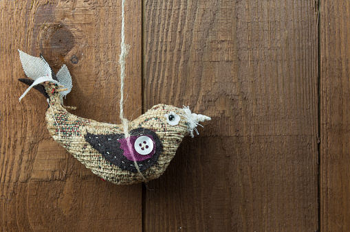 Hanging bird decoration on a wooden background with copy space. Handmade craft bird made in fabric with embellishments hanging from twine.