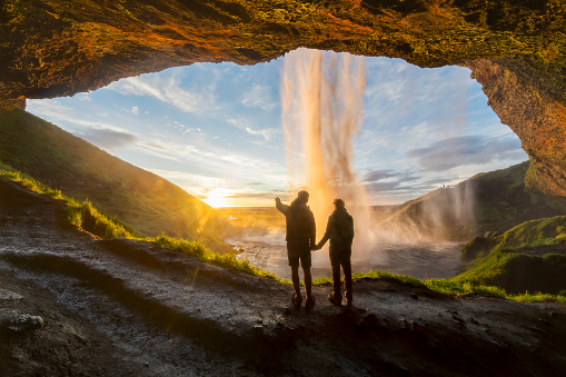 Couple under the waterfall, man pointing with finger to the sun
