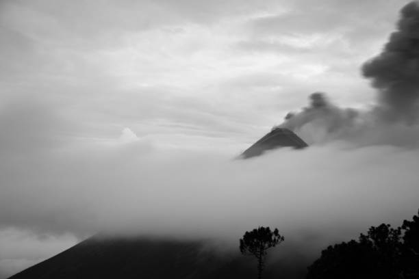 Black and white photograph of the Volcan de Fuego, erupting between the clouds.