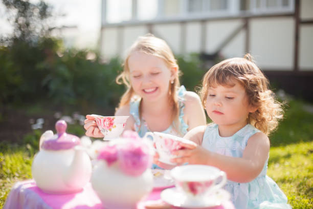 dos hermanas jugando partido de té al aire libre. - tea party little girls teapot child fotografías e imágenes de stock