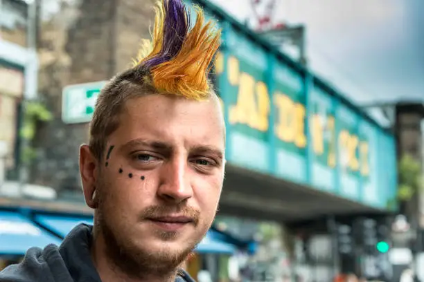 Punk Male with crested hairstyle, in the back the Camden Lock sign at the entrance of Camden market.
