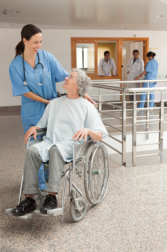 Nurse laughing with old women sitting in wheelchair in hospital corridor