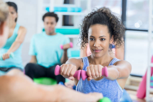 istock Serious young woman uses hand weights during exercise class at gym 847774070