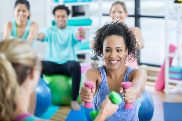istock Young woman reaches forward with hand weights during exercise class 847774074