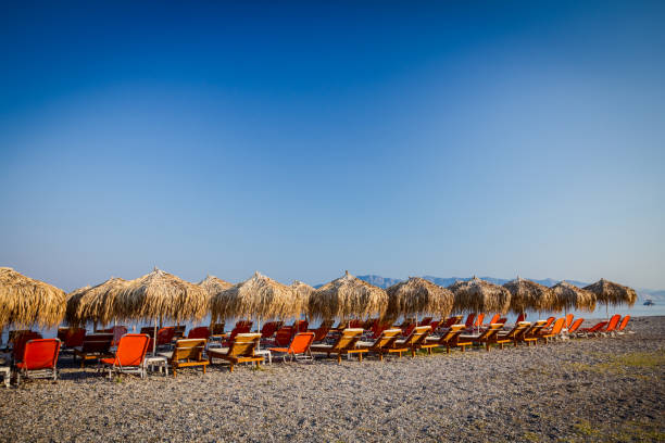 Thatched umbrellas with plastic loungers next to the coastline Sunshades made of straw, umbrellas and plastic deckchairs for a perfect holiday. thatched roof hut straw grass hut stock pictures, royalty-free photos & images