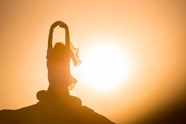 Woman in cross-legged position meditating over rocks in nature