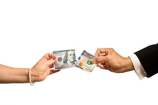 Close-up of a hand of a middle aged man and woman. They are fighting, disputing, and struggling over a US $100 bank note. The hands are pulling and tearing apart the money. The struggling relationship and divorce, and the fight for fairness. Photographed isolated on white background.