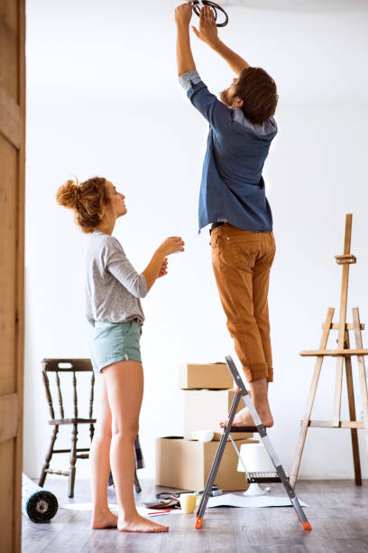 istock Young couple moving in new house, changing a light bulb. 847804744