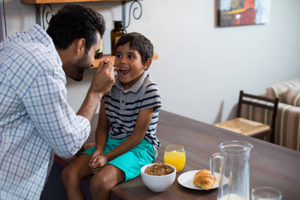 istock Happy father feeding cereal breakfast to son sitting on table 847828992