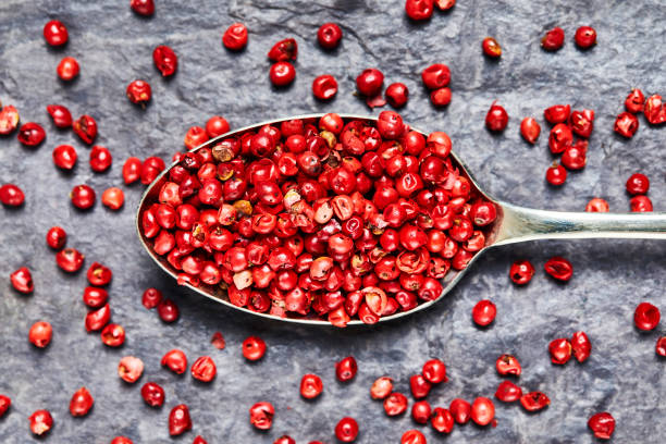 flat lay of pink peppercorns in spoon on slate background - pink peppercorn imagens e fotografias de stock