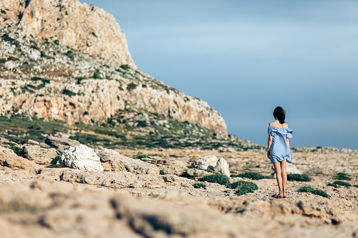 Back view of lonely woman walking on rocky desert with dramatic sky