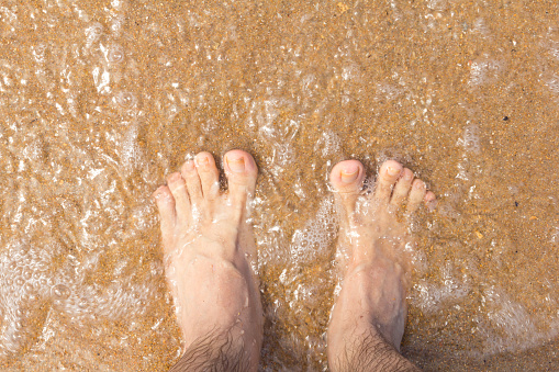 POV. Traveler photographs the feet in the sand of the beach. Crystal clear water.