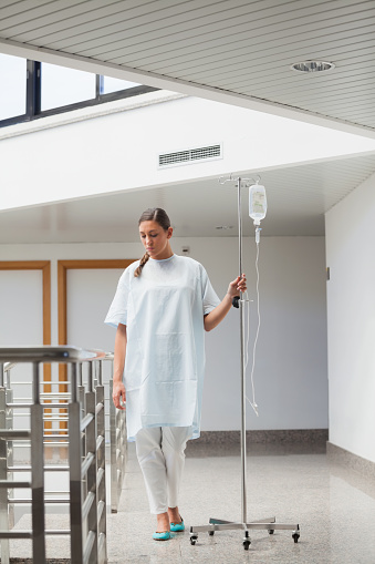 Female patient walking while holding a drip stand in hospital ward