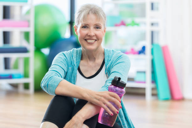 sonrisas de mujer senior para cámara durante rotura de agua en el gimnasio - aerobics beautiful bottle body fotografías e imágenes de stock