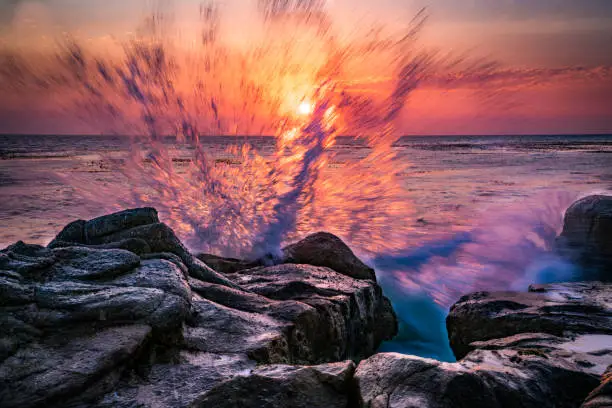 Waves crashing on the rocks with the sunset in the background